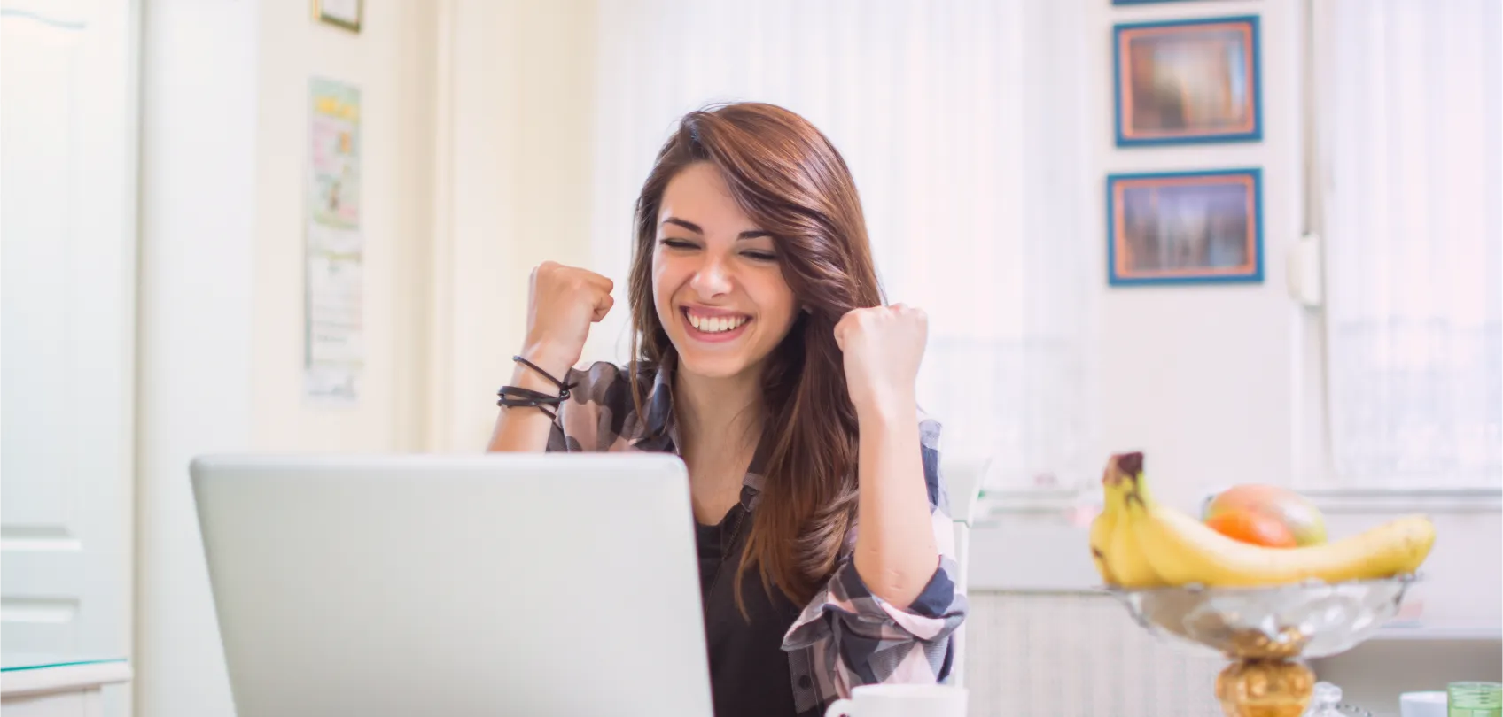 Smiling young woman celebrating in front of her laptop, symbolizing the success of having a smart website that works for the business.