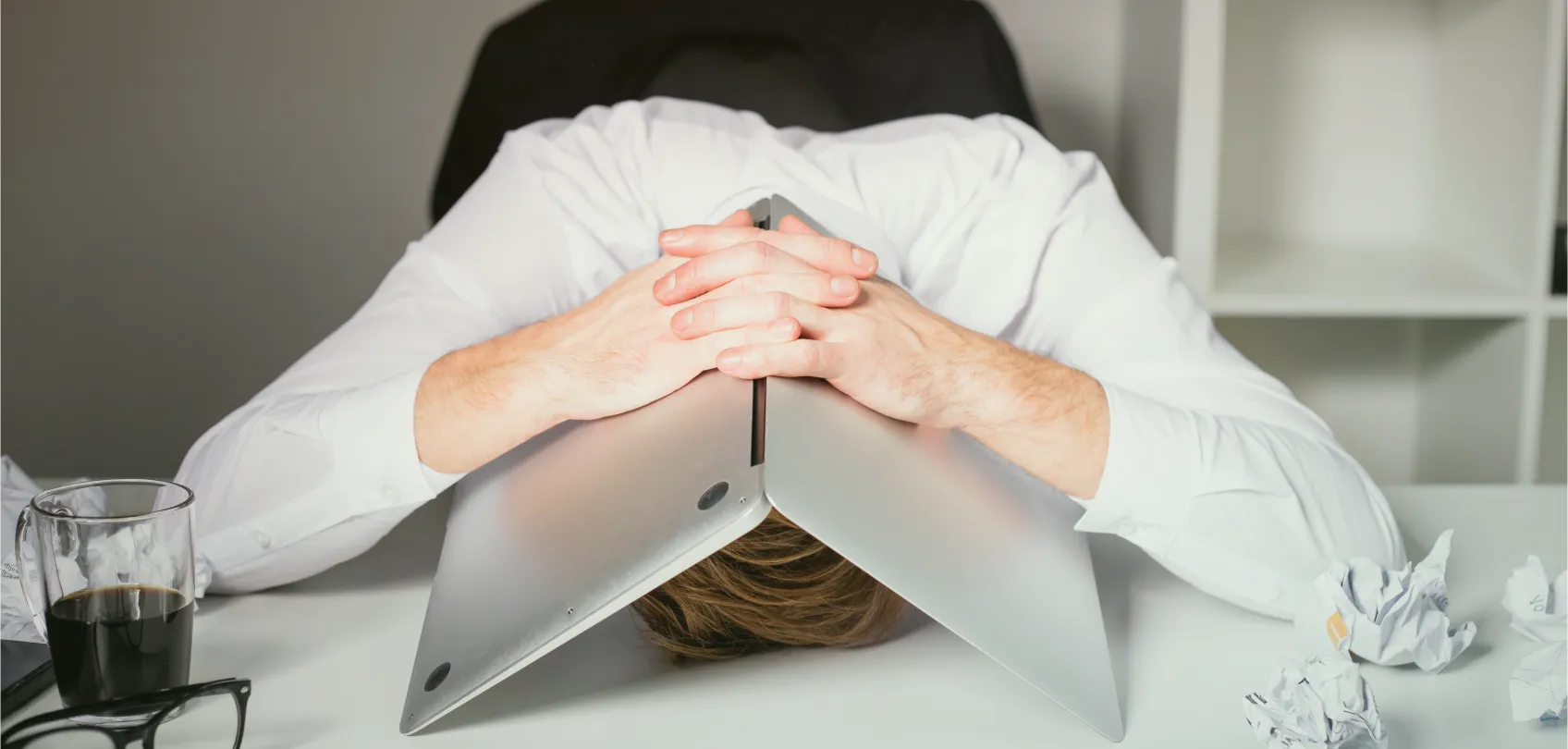 Frustrated person at their desk holding a laptop over their head, representing the problems in poorly managed web projects.
