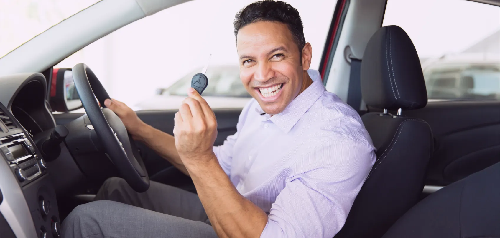 Happy customer sitting in their new car, proudly showing the key with a satisfied smile.
