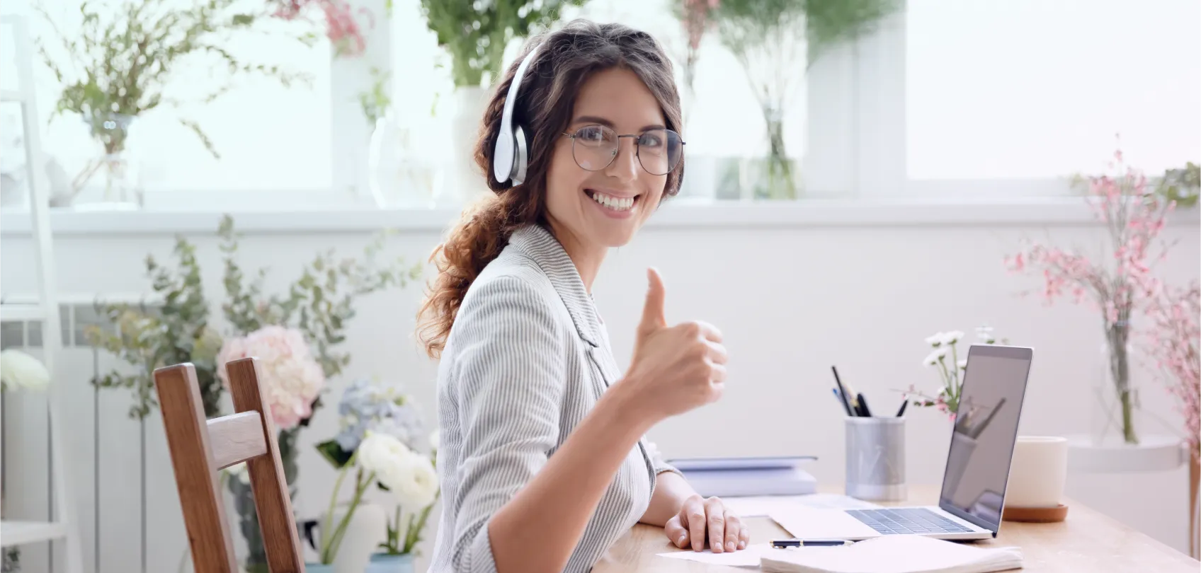 Smiling professional wearing headphones, working on a laptop and giving a thumbs-up, symbolizing the efficiency of Headless CMS compared to traditional ones.
