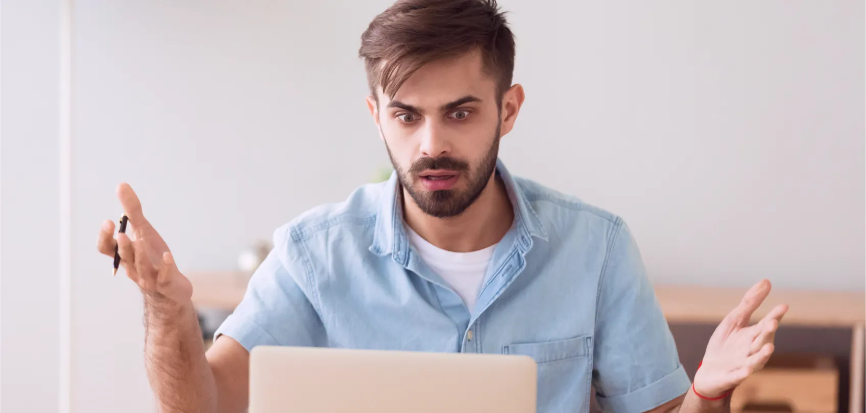 Man looking surprised in front of a laptop, representing frustration when dealing with Internet trolls.