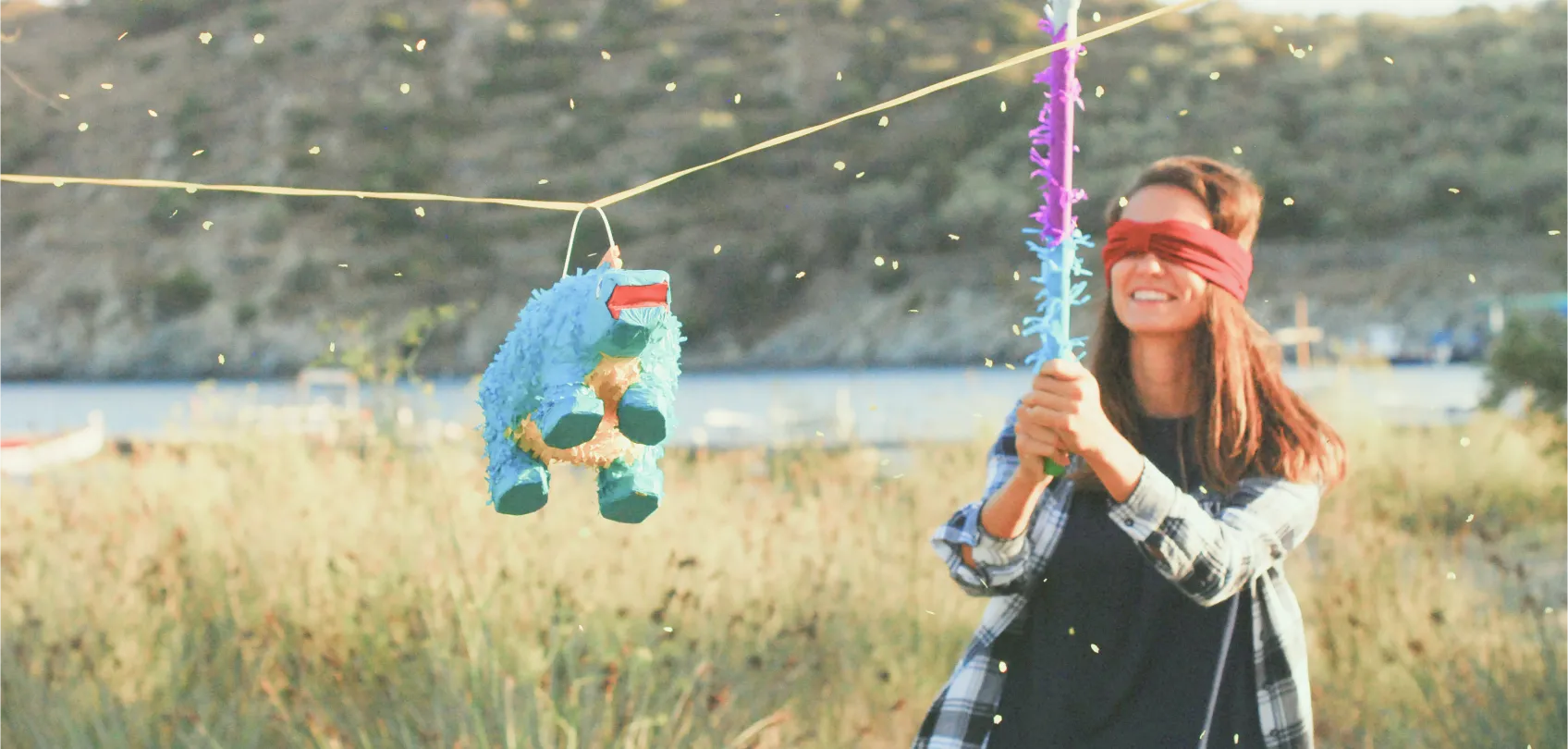 Blindfolded woman trying to hit a blue piñata in an open field, representing the metaphor of working blindly.